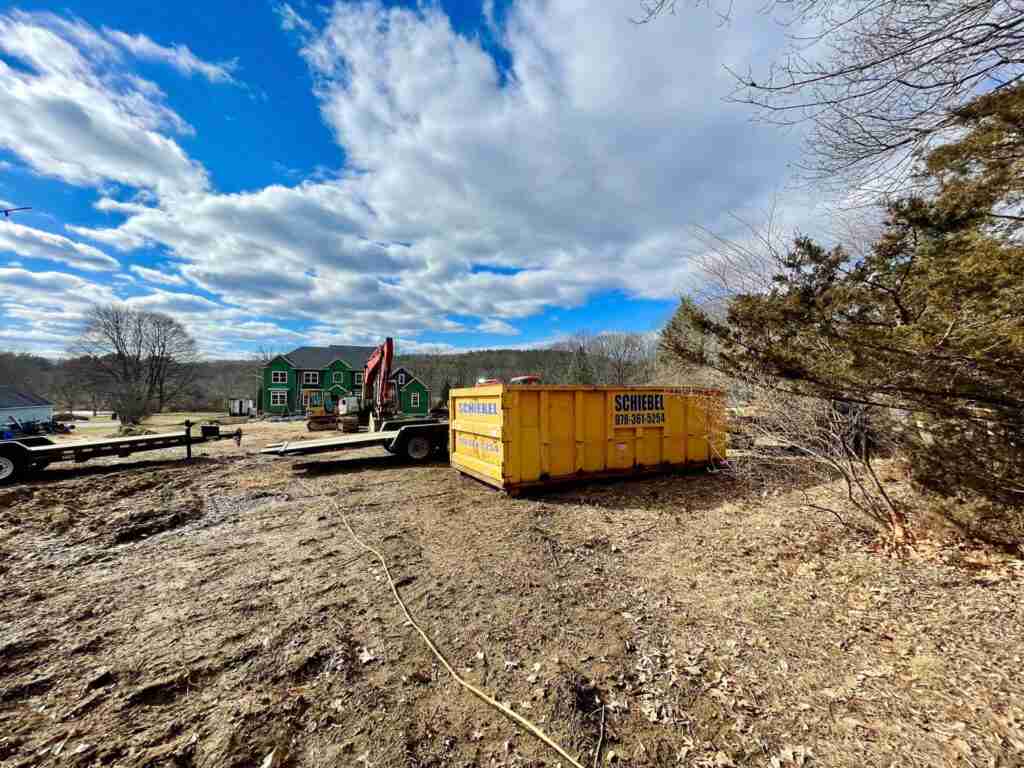 A yellow scheibel waste roll off dumpster placed at a construction site