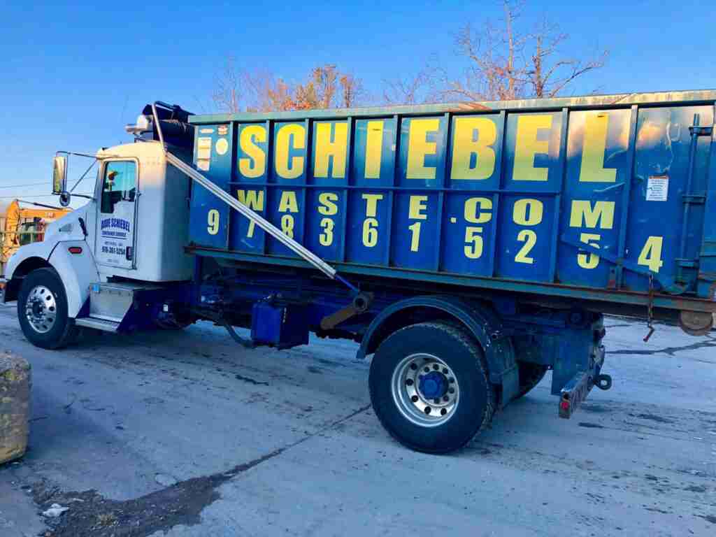 A white schiebel waste truck hold a large blue scheibel waste branded dumpster rental