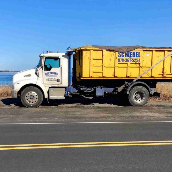 A white schiebel waste truck carrying a large yellow roll off dumpster